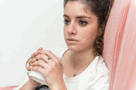 黑发，体贴的年轻女子坐在沙发上拿着一个杯子。