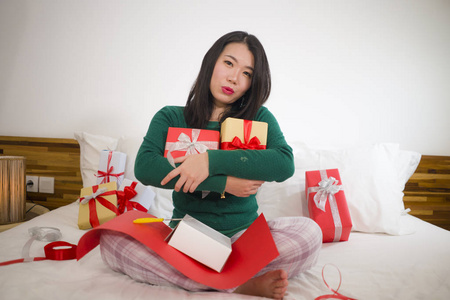 圣诞假期生活方式画像年轻快乐和甜蜜的亚洲韩国妇女坐在床上准备圣诞礼物包装礼品盒和添加丝带