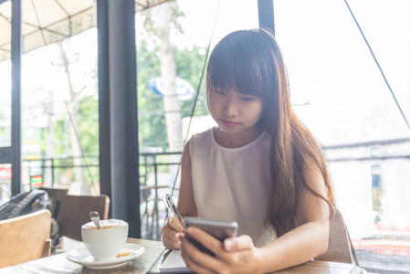 亚洲女孩用智能手机写笔记