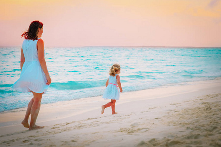 日落时分，母亲和小女孩在沙滩上散步，全家度假