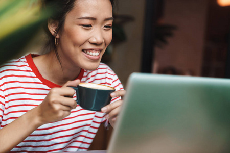 亚洲妇女喝咖啡和使用笔记本电脑的肖像