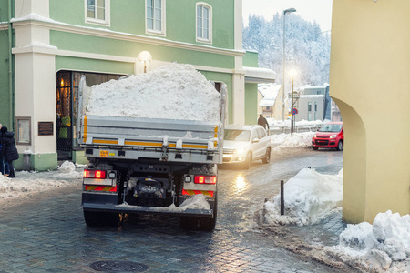 满载积雪的大型自卸车驶过欧洲古城历史中心的狭窄街道。重型机械除雪。市政服务清洁和维护城镇道路