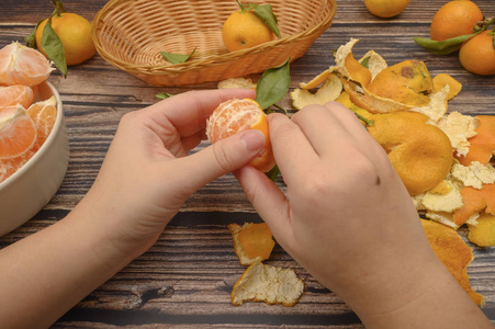 女孩的手正在擦橘子,绿叶嫩枝上的橘子,陶瓷盘子里剥皮的橘子,木制