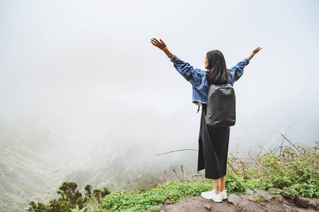 背着背包的年轻女游客在山顶上放松，欣赏雾谷的景色