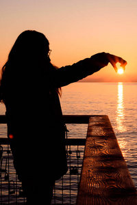 太阳升起时,背光女孩用手抓着太阳照片