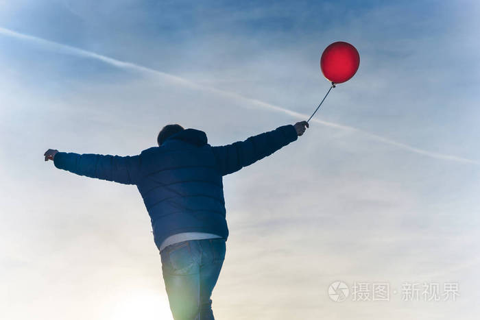 在寒冷的日子里背着一只红色气球的男人在蓝天下