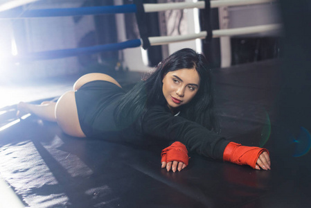 手拿红色运动绷带的性感女孩躺在拳击台上。广告培训室，运动生活方式。拳击台上性感的斗士女孩。长发女健身模特。属性