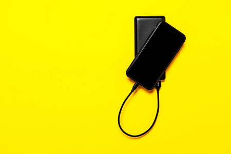 黑色电力银行为孤立在黄色背景下的智能手机充电