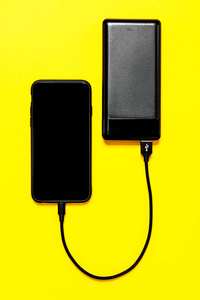 黑色电力银行为孤立在黄色背景下的智能手机充电