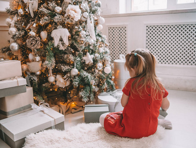 漂亮的小女孩在圣诞树旁边。美丽的女孩穿着衣服在圣诞树旁等待假期。小公主