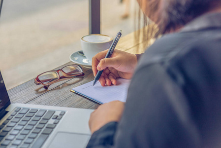 Close up of freelance woman hand writing notebook beside laptop 