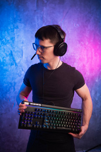 电脑呆子在彩色的粉红色和蓝色霓虹灯照亮的墙上用键盘