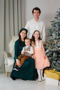 圣诞树上的年轻幸福家庭。父母和他们的孩子庆祝新年。新年房在家。圣诞节好心情。生活方式，家庭和假期。