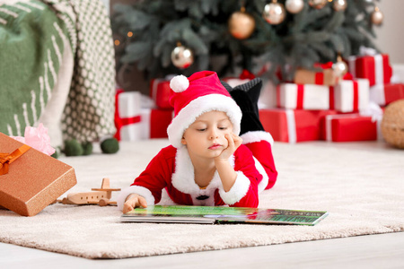 圣诞夜，一个可爱的小男孩穿着圣诞老人的服装，带着书在家里
