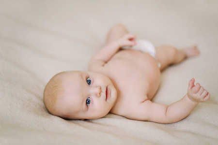 Funny little baby wearing a diaper lying on a white knitted blan