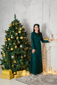 一位身穿绿色连衣裙的漂亮年轻女子站在圣诞树旁。新年房在家。圣诞节好心情。生活方式，家庭和假期。