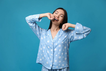 Beautiful Asian woman in pajamas stretching on blue background. 