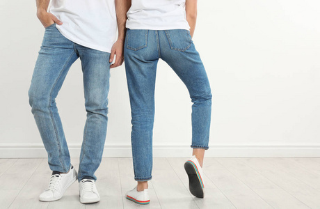 一对穿着时髦牛仔裤的年轻夫妇，靠近白墙，特写