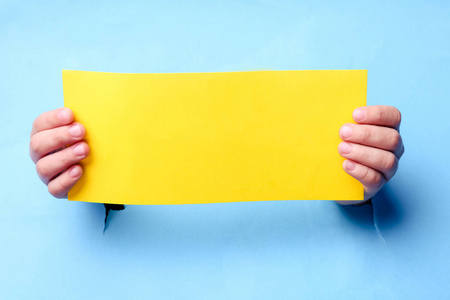 Childrens hands are holding a blank yellow sheet of paper 
