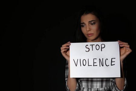 Abused young woman with sign STOP VIOLENCE on black background, 