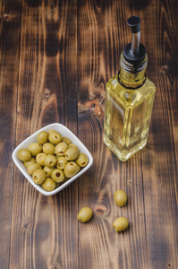 Glass bottle of olive oil and olive in a white bowl on a wooden 