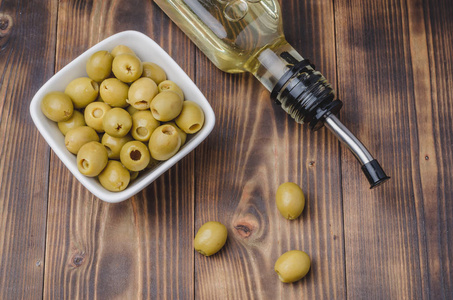 Glass bottle of olive oil and olive in a white bowl on a wooden 