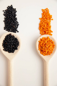 一张白色的桌子上放着两个装满橙色和黑色扁豆的木勺，旁边散落着豆子。蛋白质来源