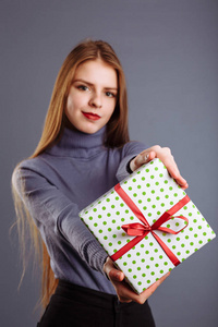 Young caucasian lady with long hair is giving a gift box to you 