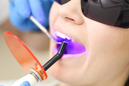 一位戴着黑色眼镜的金发女人正在接受口腔科医生的紫外线检查。选择性聚焦