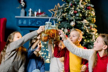 一群孩子在圣诞树的背景下，喝着柠檬水，敲着玻璃杯，聚精会神地盯着玻璃杯