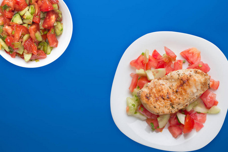 Grilled chicken breast with tomato salad, cucumbers and onions. 