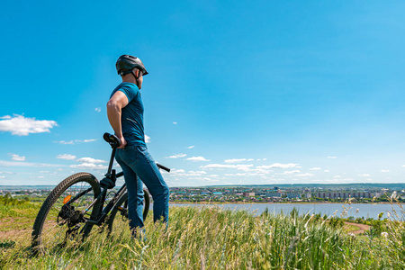 一位骑自行车的男性站在山上，看着城市。一个戴着头盔，骑着自行车，背对着摄像机的人。