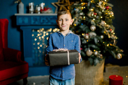 一个漂亮的小男孩拿着新年礼物放在圣诞树的背景上。