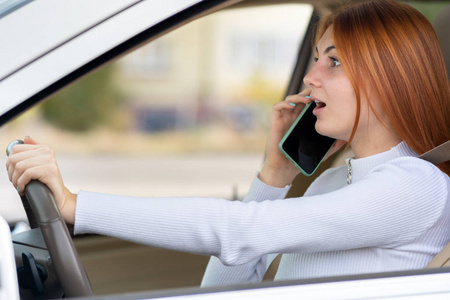 Happy redhead girl talking on her mobile phone behind the wheel 