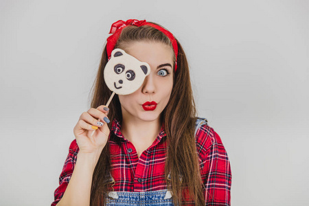 快乐的傻女孩把眼睛藏在熊猫棒棒糖后面,摆姿势,微笑,做鸭子脸.照片