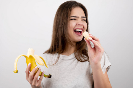 在孤立的白色背景下营养学和营养学穿着泳装和蓝色短裤的女人抱着香蕉