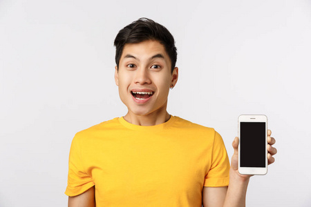 你手机里一定有。开朗兴奋的亚洲年轻人，穿着黄色t恤，展示智能手机和微笑，喜欢应用程序中的新过滤器，推荐加入公司，使用在线功能，
