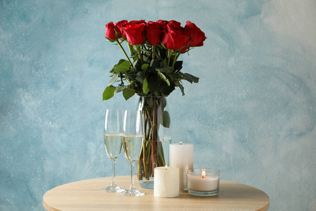 Vase with red roses, glasses of champagne and candles on wooden 