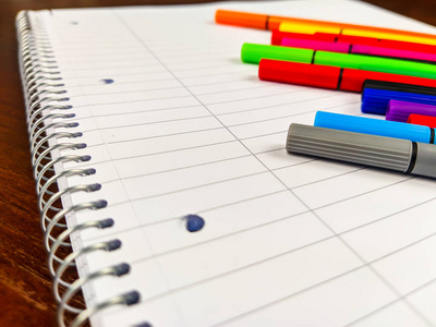 笔记本螺旋形和彩色钢笔的特写镜头，放在一个有线条的空白白色笔记本上，用于在学校学习或商务中记笔记