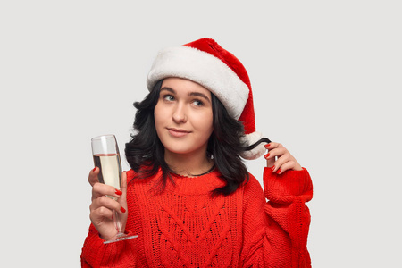 漂亮的黑发女孩，穿着红色毛衣，戴着圣诞帽，手里拿着一杯香槟。