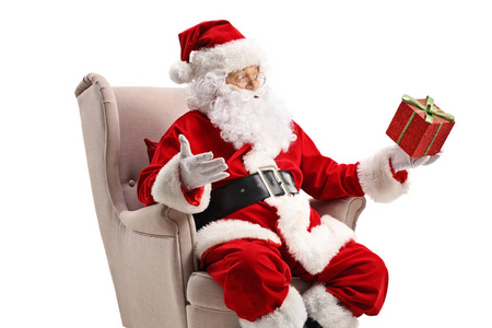 圣诞老人坐在扶手椅上拿着一个礼品盒