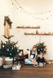 妈妈和她的小女儿坐在家里一棵圣诞树旁的地板上玩耍