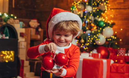 快乐的孩子穿着圣诞老人的衣服，装饰着圣诞树上的饰品。圣诞节概念。圣诞老人帮手孩子们。
