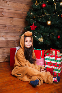 穿着睡衣的有趣小女孩拿着礼品盒坐在圣诞树旁