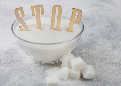 Glass bowl of natural white refined sugar with cubes on light ta