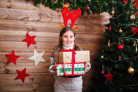 可爱的小女孩拿着礼物盒在家里的树旁。