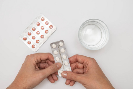 妇女服药，女性手拿白色药丸水泡，白色桌子上有胶囊和一杯水，保健和流感治疗概念