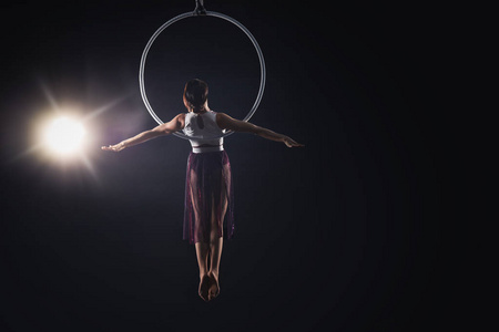 Young woman performing acrobatic element on aerial ring against 