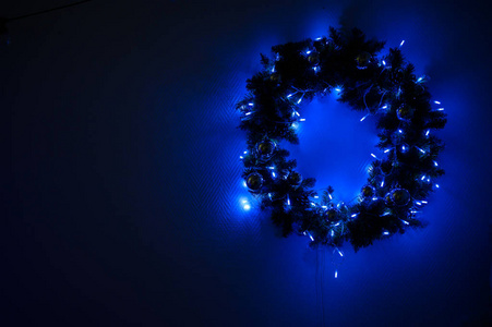 在黑暗的工作室里，挂在墙上用灯装饰的圣诞花环。新年前花环闪闪发光。