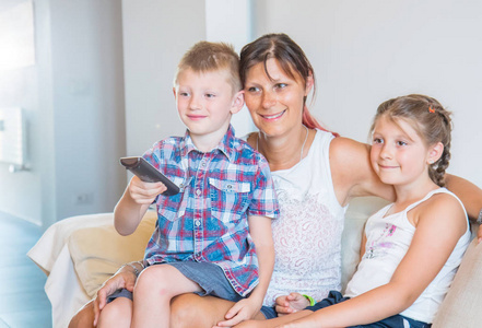 Mother and her sons are watching tv while sitting on a couch at 